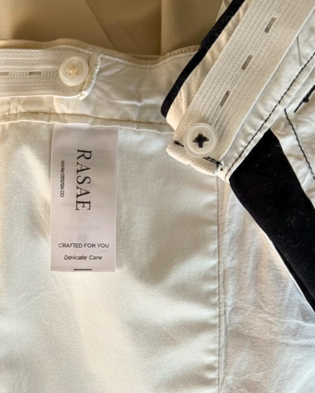 Close-up of a beige garment with a 'RASAE' label on a beige background